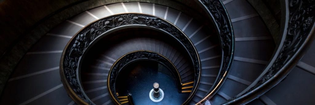 View downwards from top of dark coloured spiral staircase with ornate banister